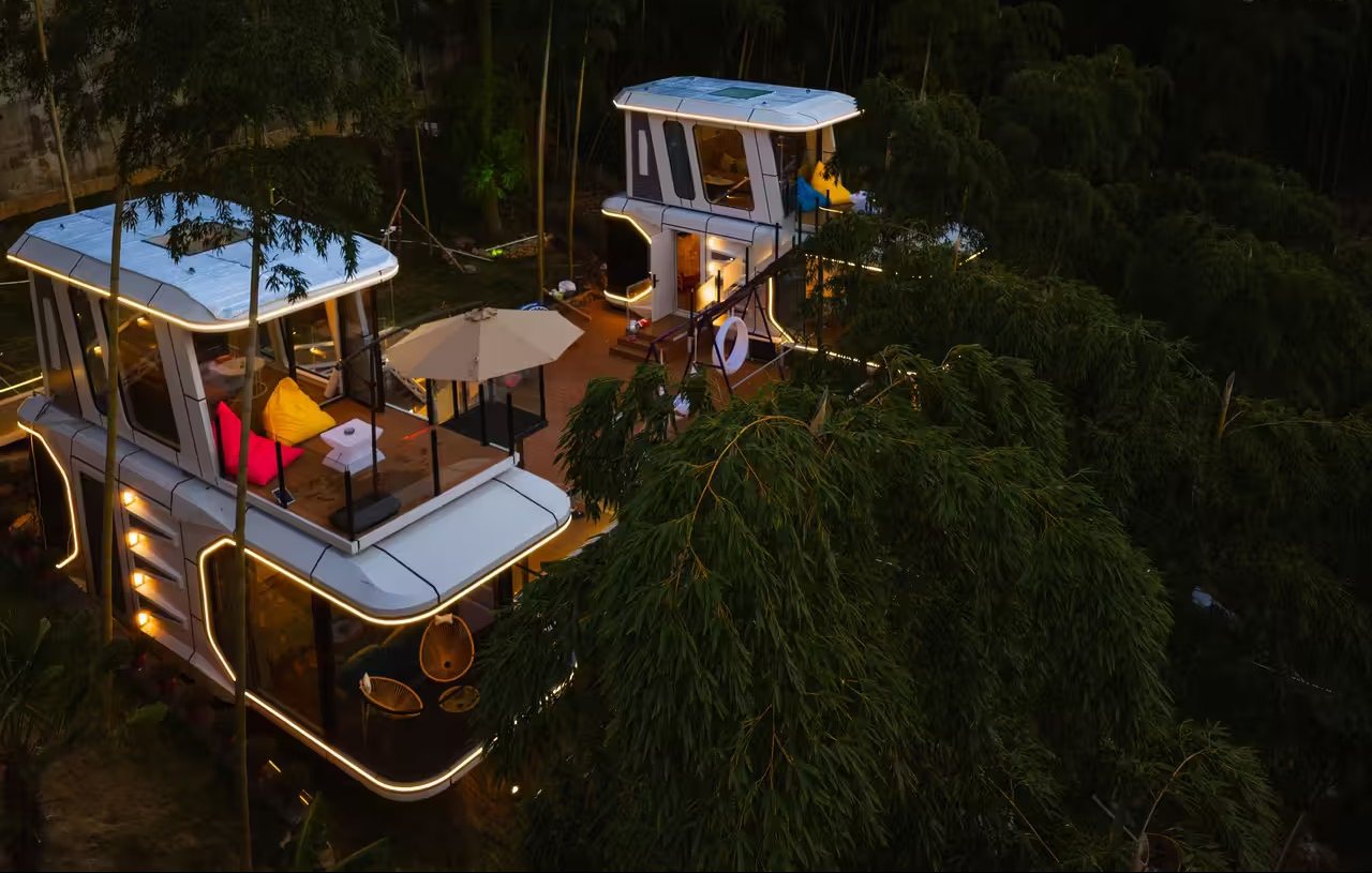 Two illuminated capsule cabins with rooftop decks in a wooded setting at night