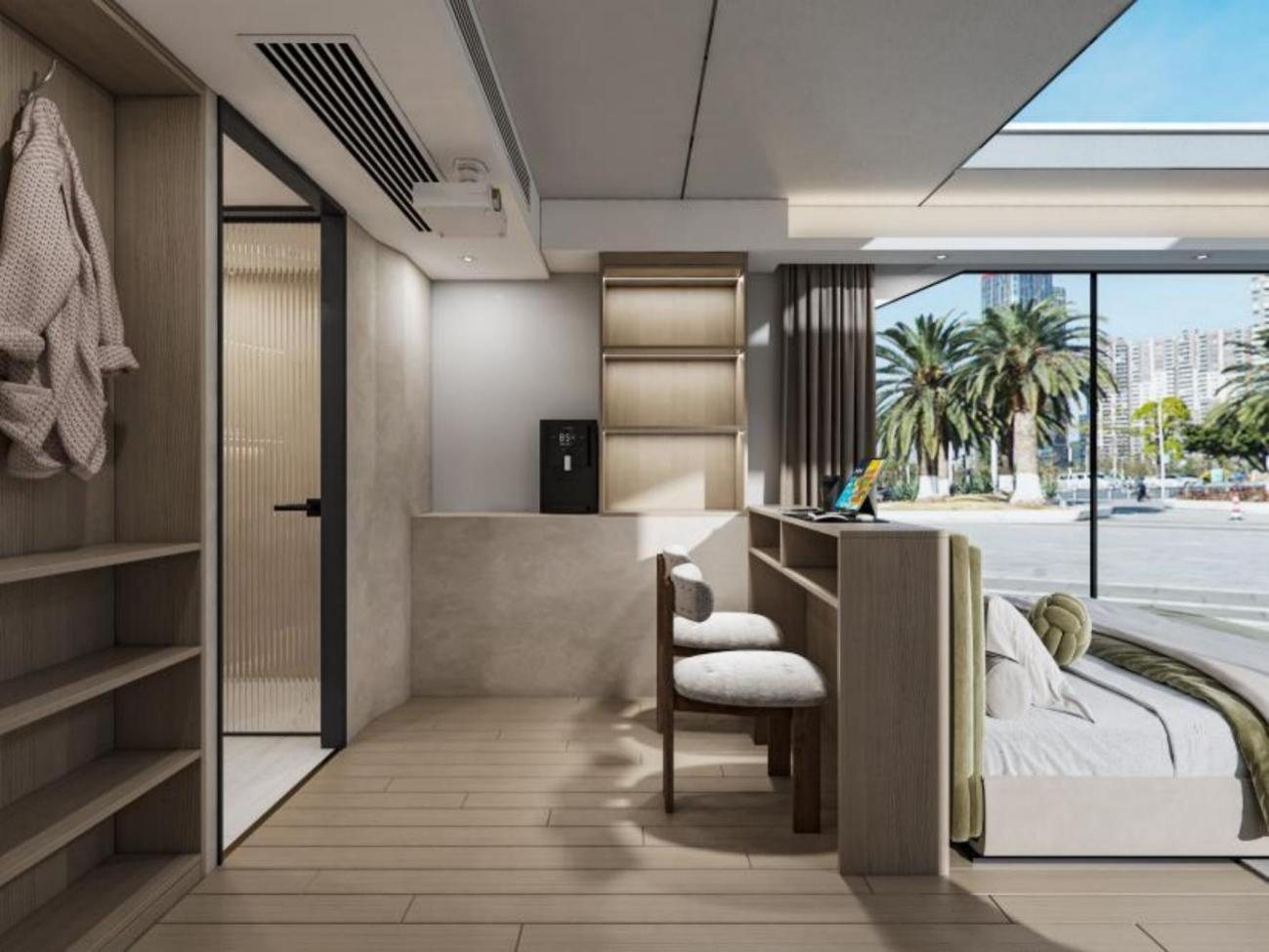 Capsule cabin interior with bed, desk, shelving, bathroom door, and large window